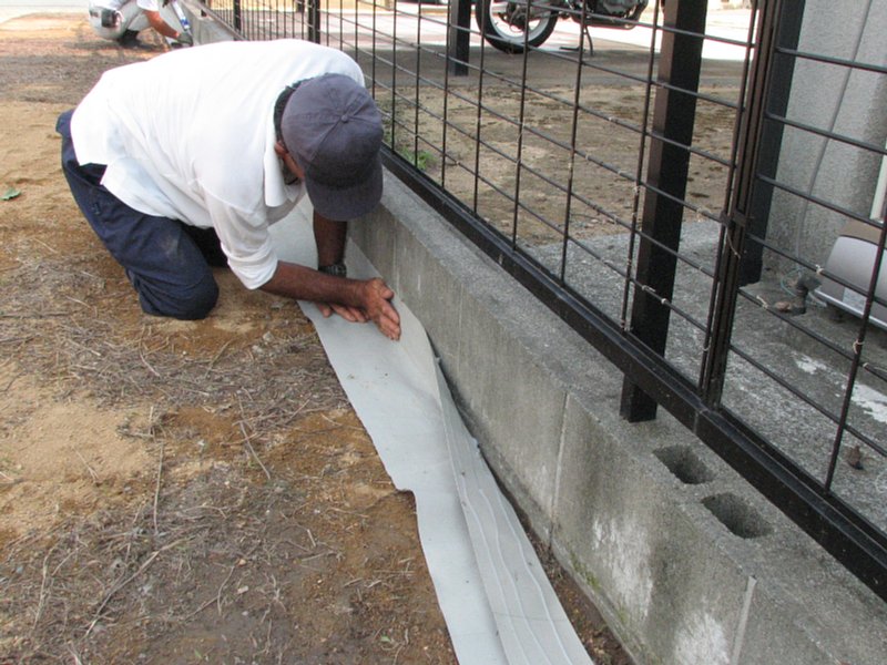 敷設中、シートに接着剤を塗り、ブロック塀に貼り付け。