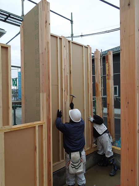 ヘビーウォールは、間取りに合わせて断熱材を組み込んだパネルを工場で一貫生産。・現場で室内側からはめ込む。・枠材から釘で留める。・一工程で構造（耐力）と断熱が完了。